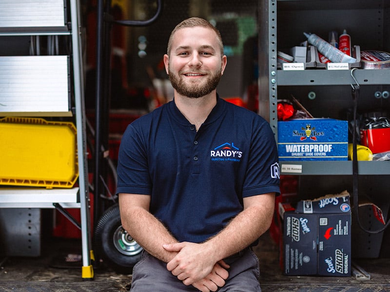 A man wearing a shirt with Randy's logo stands in front of organized tools and equipment.