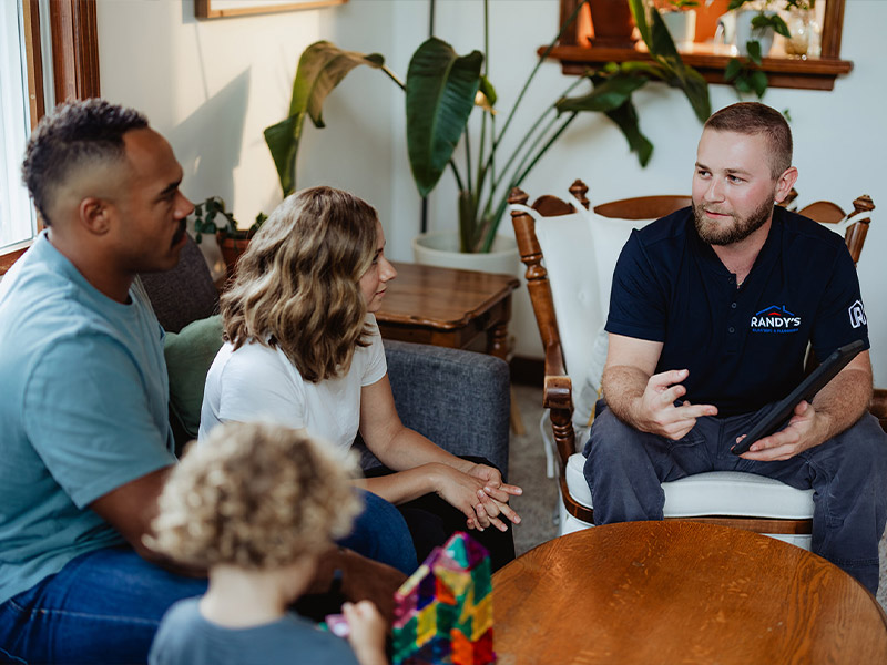 A group of people sitting in a living room discussing with a man in a Randy's shirt.